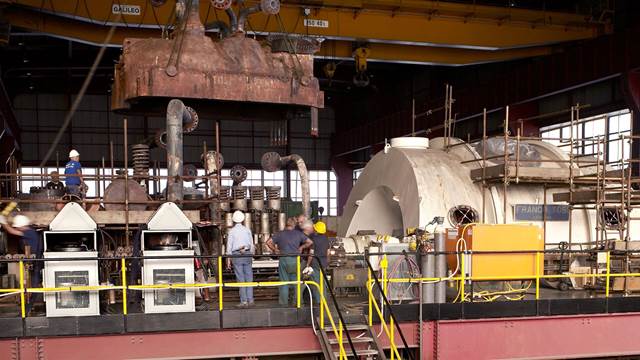 Workers disassembling a large turbine casing in an industrial facility
