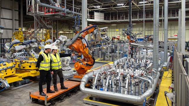 Robotic manufacturing line with workers inspecting equipment, demonstrating the use of clean and precise induction bonding technology in automated production.
