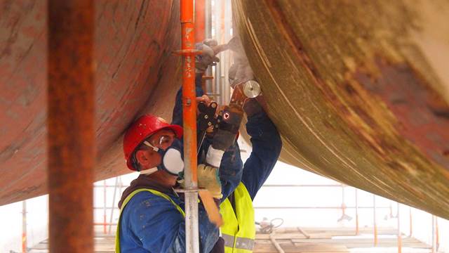 Industrial worker using induction heating system for coating removal on large steel structure   