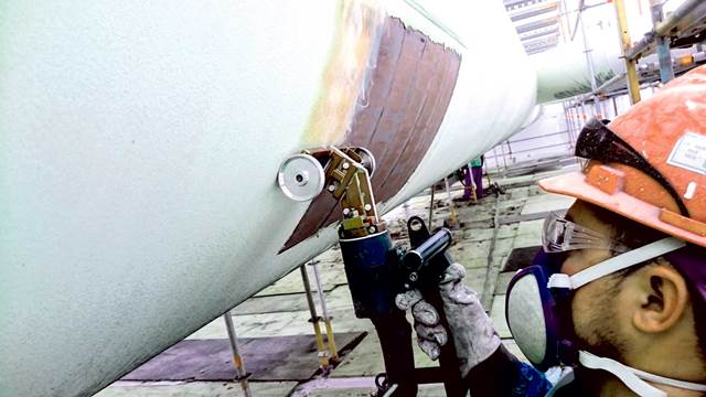 Operator using handheld induction heating system for pipeline coating removal