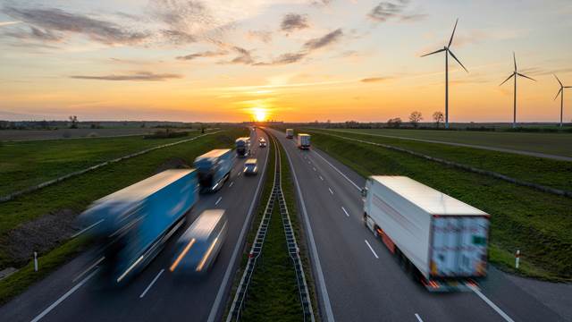 Trucks and vehicles on a motorway at sunset with wind turbines in the background, representing induction heating applications across automotive, renewable energy and transport industries at ENRX