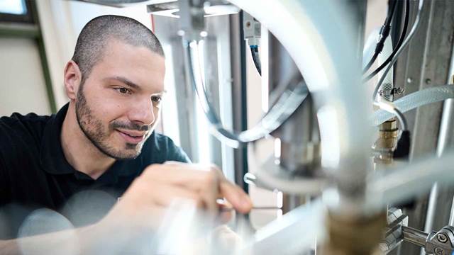 Technician adjusting components on clean, precision induction heating equipment inside an industrial setting.