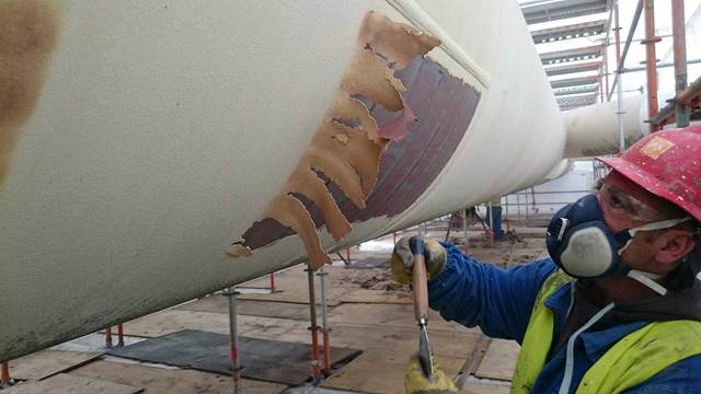 Worker removing coating from pipeline using induction heating coating removal system