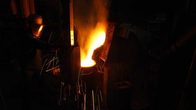 Operator pouring molten metal from an induction melting furnace in an industrial environment