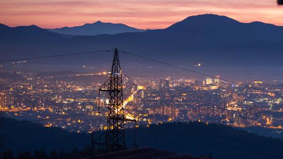 Stromleitungsmast vor der Silhouette einer Skyline bei Dämmerung, der für nachhaltige Energietechnologie steht