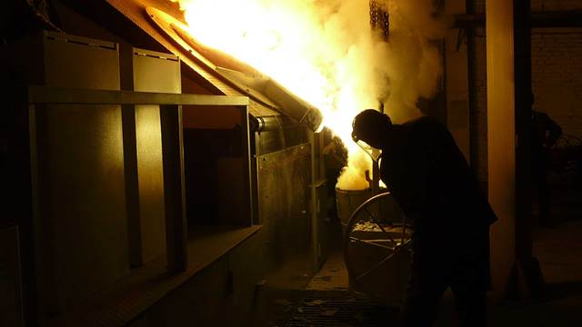 Operator pouring molten metal from an induction melting furnace in an industrial foundry