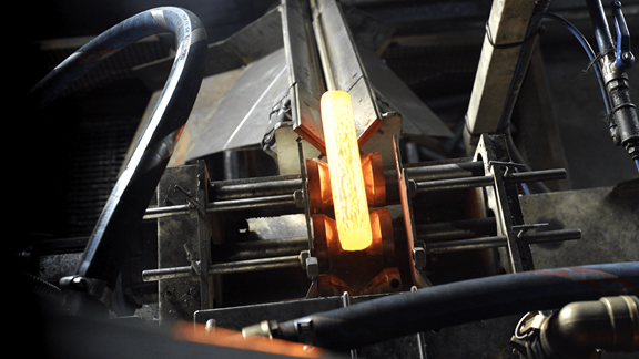 Close-up of a heated metal billet glowing orange during induction heating in a forging machine inside an industrial setting