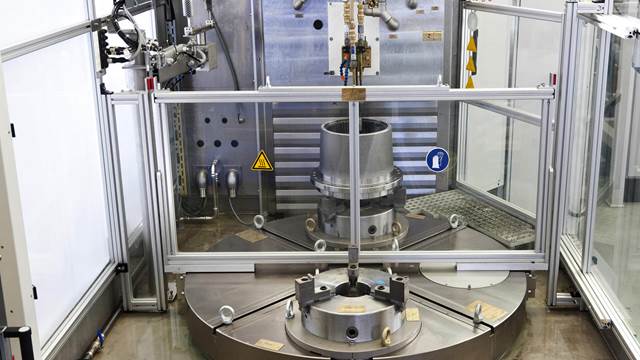 Induction tempering station processing an industrial metal component with controlled heating inside a protective enclosure.