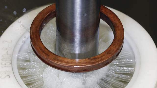 Close-up of a small gear being quenched after induction heating during a hardening process, with water spray visible around the component