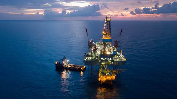 Offshore oil and gas platform with support vessel at sunset