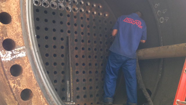 Worker inside an industrial boiler performing boiler tube extraction, surrounded by tube sheets and using tools to remove worn tubes.
