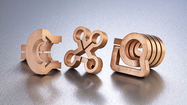 Three 3D‑printed copper induction coils of different shapes placed on a metallic surface, designed for precision heating in industrial applications