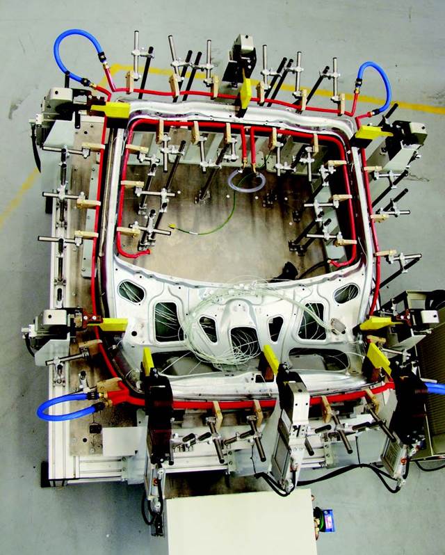 Top view of an early induction bonding fixture with a single-turn copper ring coil surrounding an automotive panel, used for full-perimeter adhesive curing.