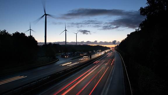 Highway with moving vehicles at sunset and wind turbines in the background, symbolizing sustainable automotive and electrotechnical applications of induction heating