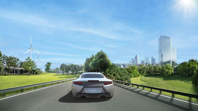 Electric car driving on a highway with wind turbines and city skyline in the background, representing sustainable applications of induction heating technology