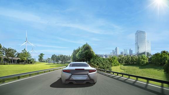 Electric car driving on a highway with wind turbines and city skyline in the background, representing sustainable applications of induction heating technology