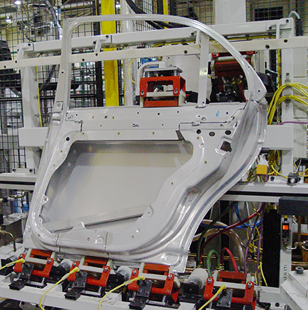 Automotive door panel on an assembly line with ENRX U-Coil® induction bonding units integrated into the output conveyor for efficient adhesive curing.