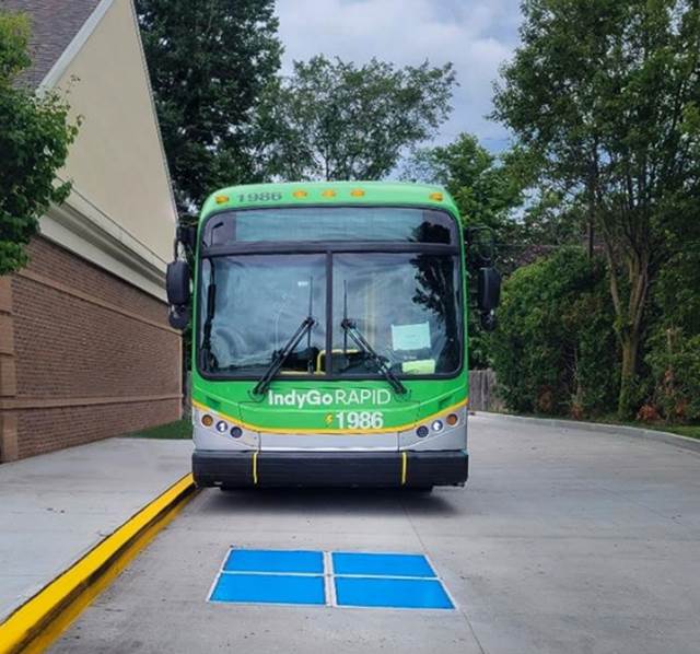 Electric IndyGo RAPID bus aligned over an ENRX wireless charging pad used for dynamic and opportunity charging on transit routes.