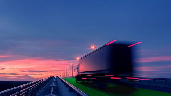 Truck driving on an electric road at sunset, illustrating ENRX dynamic wireless charging technology for heavy vehicles.