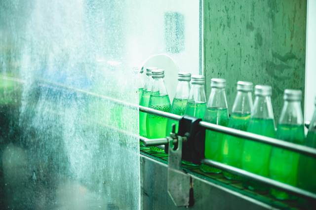 Green beverage bottles moving along an automated production line, illustrating the use of inductive power supply in bottling and packaging systems