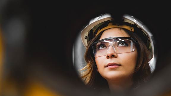 Female engineer wearing a hard hat and safety glasses looking upward on an industrial site, representing career opportunities at ENRX