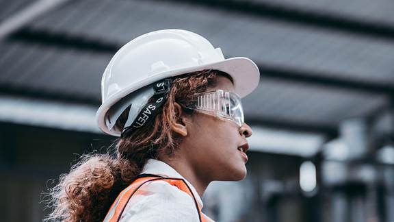 Female industrial worker in a white hard hat, safety glasses and high-visibility vest, representing safe and clean working conditions enabled by induction heating at ENRX