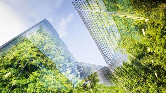 Double exposure of modern glass buildings and green trees, symbolising how induction heating reduces carbon footprint in industrial operations at ENRX