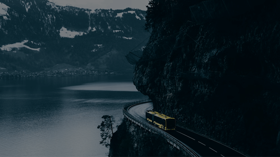 Un bus jaune naviguant sur une route de montagne spectaculaire le long d'un fjord au crépuscule, illustrant la vision et le parcours d'ENRX dans la technologie de chauffage par induction