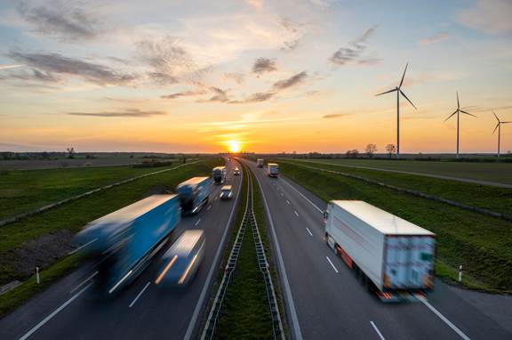 Highway with heavy transport and wind turbines illustrating ENRX industries including automotive, electrotechnical, energy, and industrial manufacturing.