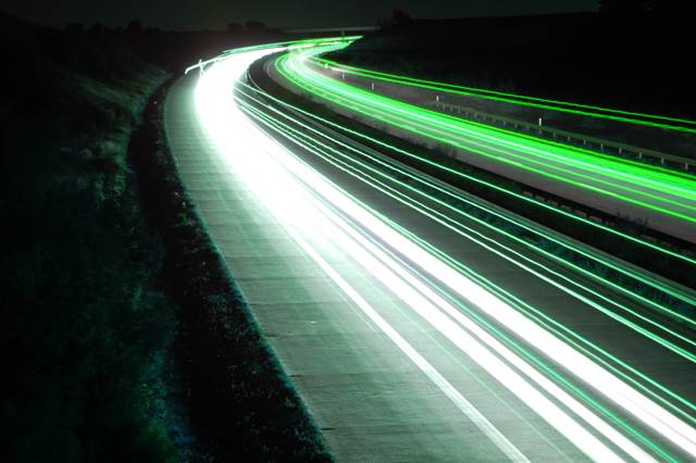 Highway at night with green and white light trails, symbolizing dynamic wireless charging for electric vehicles.