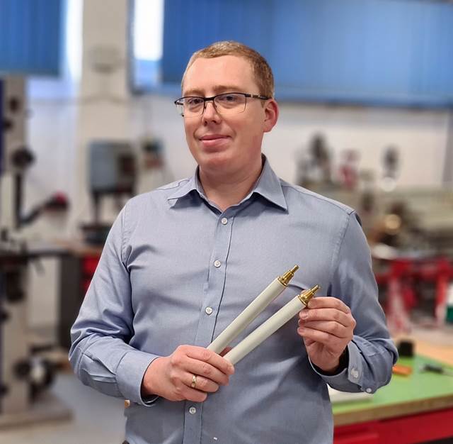 A person in a workshop environment holding two induction welding impeders used as consumables in tube and pipe production.