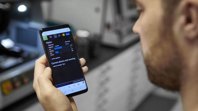 Technician checking real-time status data for ENRX Minac induction heating equipment on smartphone