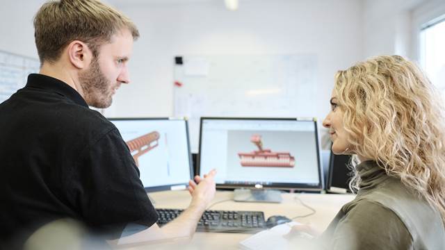 Two engineers collaborating at computer workstations while reviewing 3D simulation models of an induction coil design.