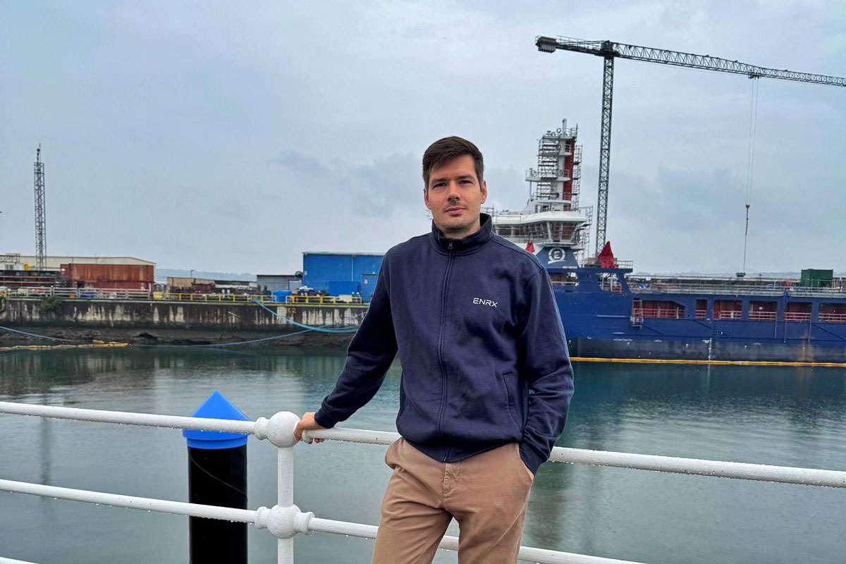 Adrian Assie, Geschäftsführer bei ENRX Spanien, steht an einem Hafen mit einem großen Schiff und Werftkränen im Hintergrund.