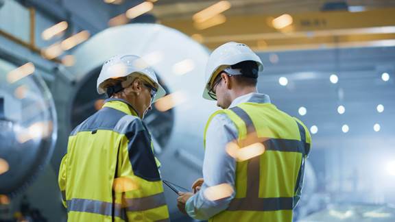 Deux ingénieurs de maintenance ENRX, vêtus de vestes haute visibilité et de casques de chantier, examinant des données sur une tablette dans une installation industrielle lourde, illustrant le service et l'assistance sur site pour le chauffage par induction