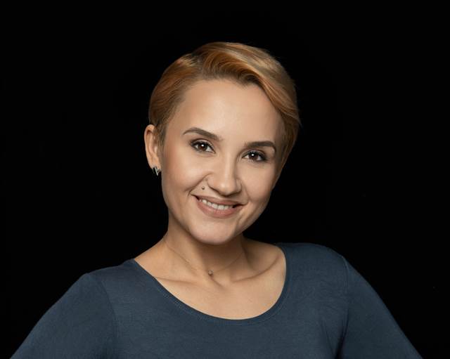 Studio portrait of Ana-Maria Maria against a black background, smiling and facing the camera. 